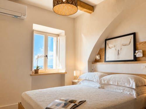 Bright bedroom at Tuscan Townhouse with sea view, wooden bed frame, white linens, and arched ceiling