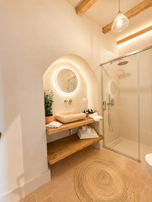 Modern bathroom at Tuscan Townhouse with illuminated round mirror, wooden sink vanity, walk-in shower, and stone flooring
