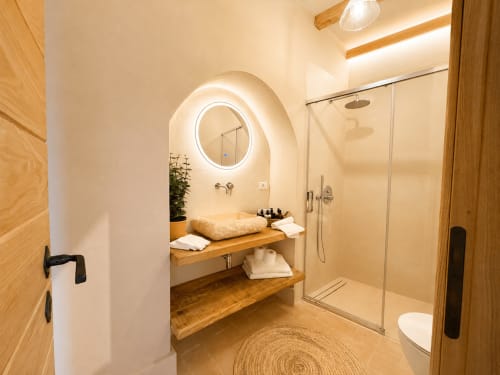 Modern bathroom in Tuscan Townhouse with circular LED mirror, wooden vanity, rainfall shower, and beige tones
