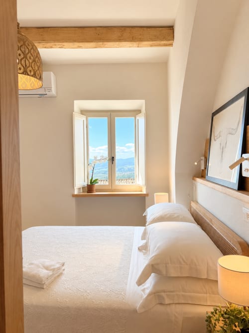 Bright bedroom in Tuscan townhouse with twin beds, window overlooking mountains, TV, and wooden beams