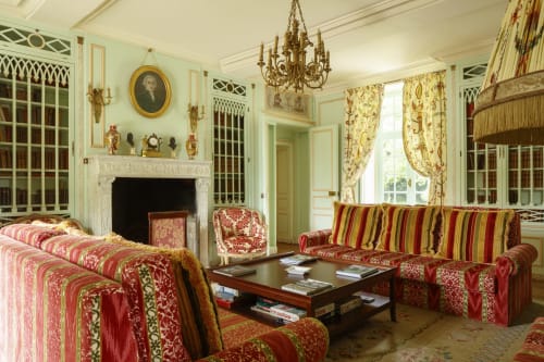 Élégant salon du Château de Servigny avec lustre orné, mobilier rayé rouge et or, cheminée et décor d'époque