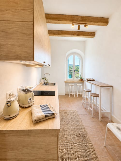 Modern kitchen in Tuscan Townhouse with wooden beams, white cabinetry, and arched window overlooking Montemassi gardens