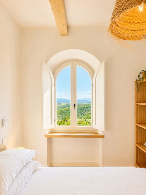 Tuscan bedroom with arched window opening to rolling green landscape and hills at Montemassi