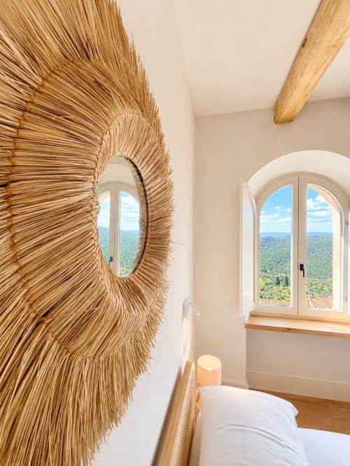 Tuscan bedroom with woven straw mirror, arched window overlooking green landscape, wooden beams, and bed at Tuscan Townhouse