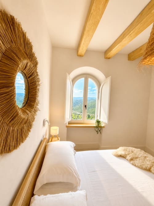 Bright bedroom in Tuscan Townhouse with arched window overlooking garden, wooden beams, and decorative woven mirror