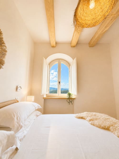 Tuscan bedroom with arched window overlooking mountains, wooden beams, white bedding, and natural light at Montemassi hotel