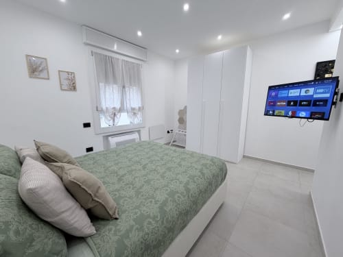 Camera moderna di Dream Suite Bologna con biancheria verde, armadio bianco, TV a parete e design minimalista