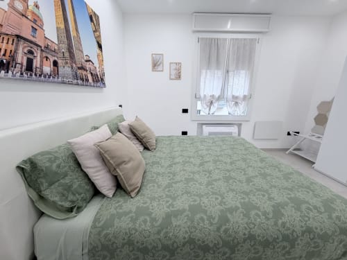 Camera moderna presso Dream Suite Bologna con biancheria verde decorata, cuscini bianchi, arte su tela della città italiana, e
