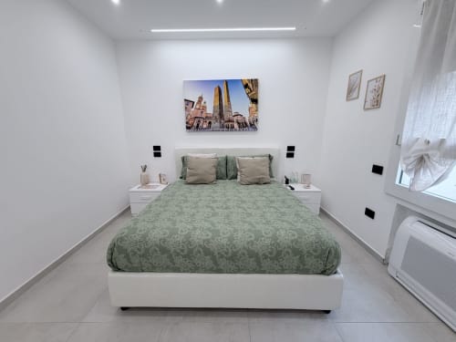 Camera da letto moderna a Dream Suite Bologna con biancheria verde decorata, comodini bianchi e opere d'arte con vedute di Bologna