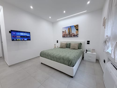 Camera da letto moderna presso Dream Suite Bologna con biancheria verde, TV a parete e opere d'arte raffiguranti le torri di Bologna.