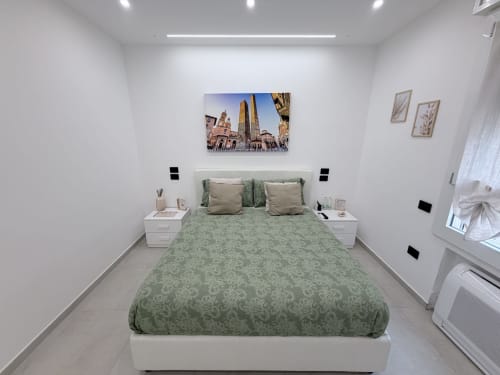 Camera da letto moderna in Dream Suite Bologna con letto a motivi verdi, comodini bianchi e opere d'arte che ritraggono il panorama di Bologna