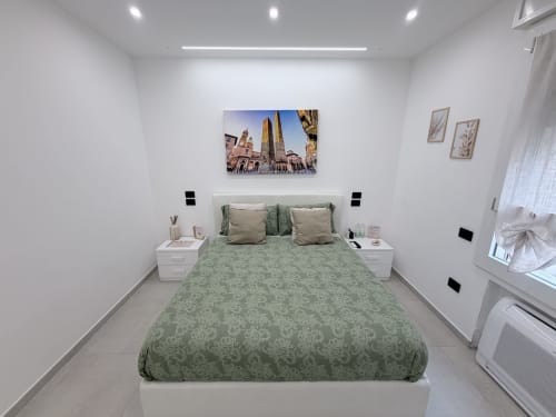 Camera moderna della Dream Suite Bologna con biancheria verde decorata, comodini bianchi e quadri dello skyline sopra il letto