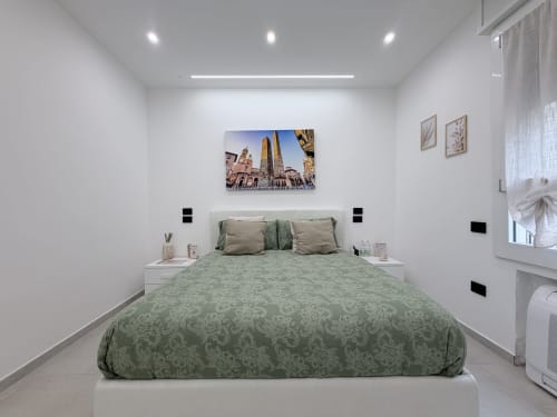Camera moderna della Dream Suite Bologna con biancheria letto a motivi verdi, comodini bianchi e artwork con paesaggio urbano sopra il letto