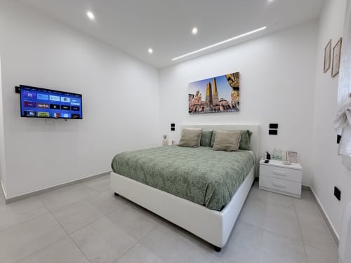 Camera moderna Dream Suite Bologna con biancheria verde, letto bianco sospeso, TV a parete e opere d'arte urbana
