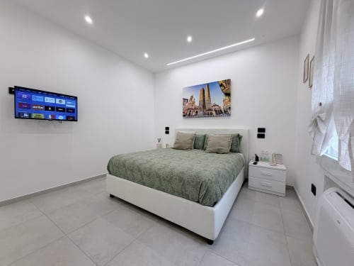 Camera moderna presso Dream Suite Bologna con biancheria verde, TV a schermo piatto, comodino bianco e pavimento in piastrelle a Bologna.