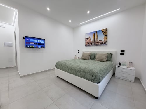 Camera moderna Dream Suite Bologna con letto trapuntato verde, TV a schermo piatto, comodino bianco e pavimento in piastrelle