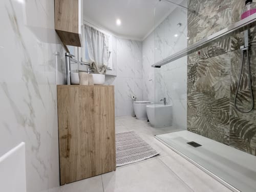 Bagno moderno nella Sabò Double Room di Dream Suite Bologna con piastrelle in marmo, mobile lavabo in legno, doccia a pioggia e bidet