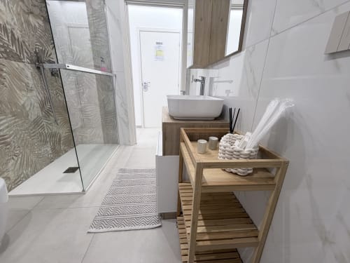 Bagno moderno nella Dream Suite Bologna con doccia in vetro, lavabo ceramico, scaffali in legno e pavimento in piastrelle bianche