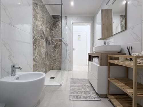 Bagno moderno della Dream Suite Bologna con rivestimenti in marmo, vasca freestanding, doccia walk-in, vanità in legno e specchio