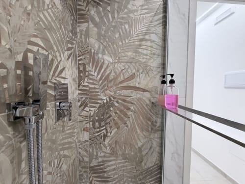 Moderna cabina doccia con piastrelle a motivo foglie tropicali e flacone di prodotti rosa alla Dream Suite Bologna