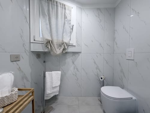 Elegante bagno in marmo nella suite Sabò di Dream Suite Bologna con wc, portasciugamani e finestra con tenda