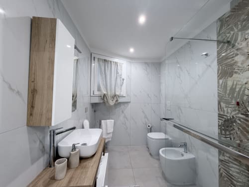 Bagno moderno nella suite Sabò di Dream Suite Bologna con piastrelle in marmo, mobile in legno, bidet, wc e doccia in vetro