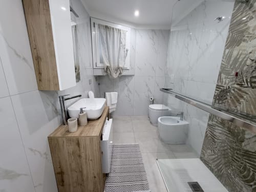 Bagno moderno della stanza Sabò a Dream Suite Bologna con piastrelle in marmo bianco, mobile in legno, toilette, bidet e doccia a filo