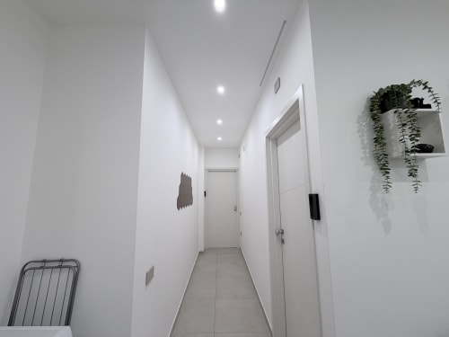 Moderno corridoio della Dream Suite Bologna con pareti bianche, pavimento in piastrelle, illuminazione incassata, piante sospese e porte delle camere