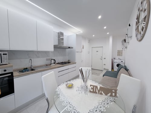 Moderna zona cucina-soggiorno della Dream Suite Bologna con arredamenti bianchi, elettrodomestici in acciaio inox, tavolo da pranzo e divano