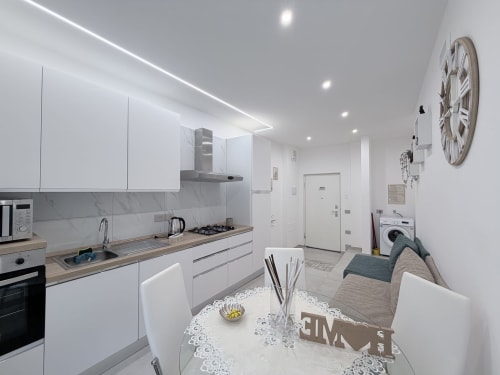 Moderna cucina bianca con piano in legno, tavolo da pranzo e zona living nella camera doppia Sabò della Dream Suite Bologna