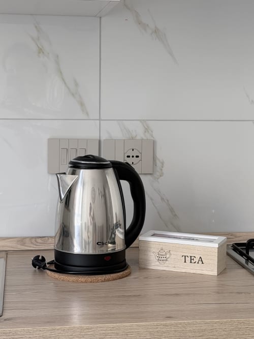 Bollitore elettrico in acciaio inox su sottobicchiere in sughero nella cucina Dream Suite Bologna con scatola di tè e rivestimento in marmo