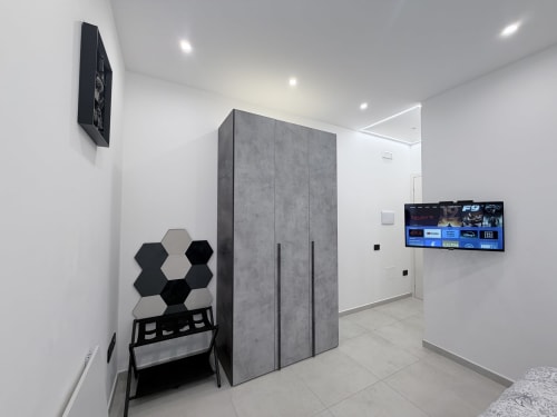 Camera moderna della Dream Suite Bologna con guardaroba grigio, arte murale esagonale, TV e design minimalista