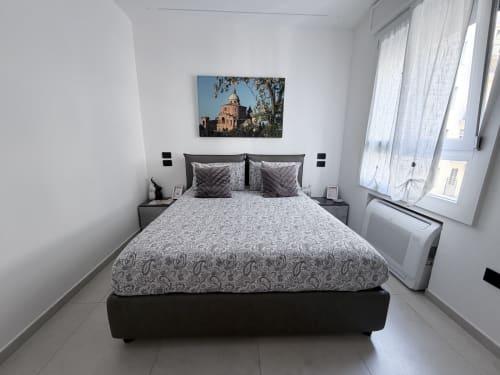 Camera moderna presso Dream Suite Bologna con letto matrimoniale, biancheria grigia e opera d'arte religiosa sopra la testata