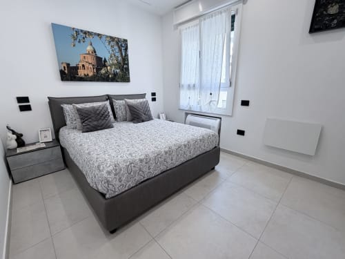 Camera moderna della Dream Suite Bologna con letto nero, biancheria grigia e bianca, pavimento piastrellato e foto architettonica sopra il letto