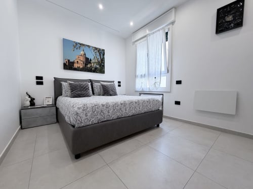 Camera moderna a Dream Suite Bologna con letto nero, pareti bianche, quadri con cattedrali e vista sulla corte interna
