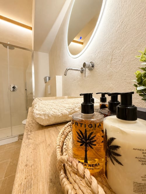 Luxury bathroom at Tuscan Townhouse with designer toiletries, curved mirror, and wooden vanity in Montemassi