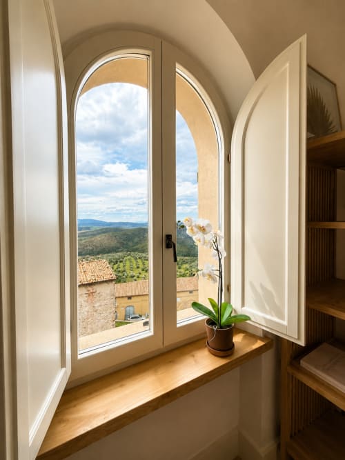 Arched window at Tuscan Townhouse in Montemassi showing rolling Tuscan hills, vineyards, and white orchid on sill