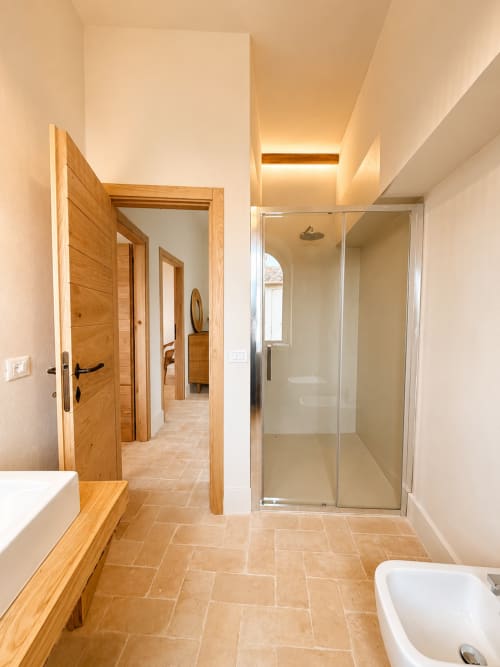 Modern bathroom at Tuscan Townhouse B&B in Montemassi with wooden doors, glass shower, terracotta floors, and ambient