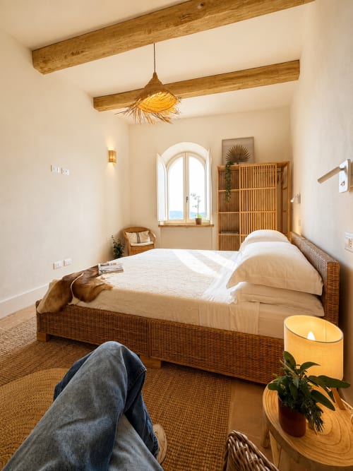 Tuscan bedroom with wicker bed, wooden beams, arched window overlooking landmark, and warm lighting at Bellavista Suite