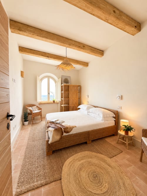 Tuscan bedroom with exposed wooden beams, wicker bed, arched window with landmark view, and natural earth-tone décor in