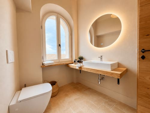 Modern bathroom in Bellavista Suite at Tuscan Townhouse with arched window, round lit mirror, white sink, and terracotta