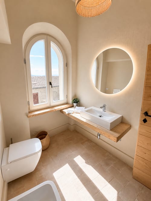Modern bathroom in Tuscan townhouse with arched window, illuminated mirror, wooden sink countertop, and countryside views