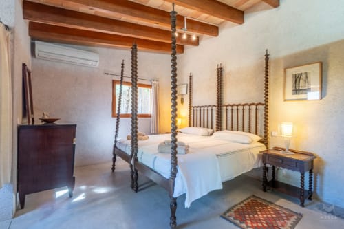 Amplio dormitorio con cama de cuatro postes de madera en Massa Properties en Artà, con techo de vigas y decoración tradicional