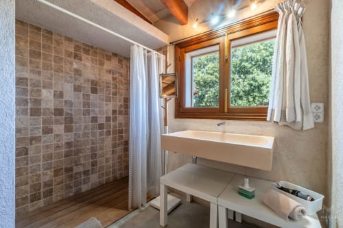 Baño moderno con ducha alicatada, lavabo suspendido, marco de ventana de madera y vigas vistas en Massa Properties, Artà