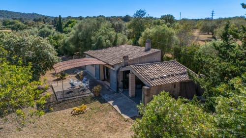Villa rústica Massa Properties en Artà rodeada de árboles mediterráneos, jardines y tejadillos de barro