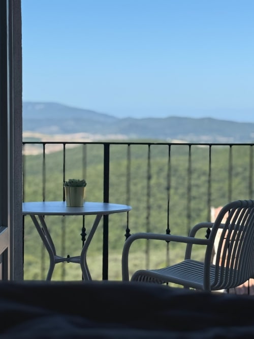 Black chair and table on Terrace Suite balcony overlooking Tuscan countryside and rolling hills at Tuscan Townhouse