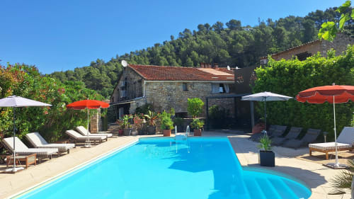 Piscine ensoleillée de la Bergerie Du Moulin avec transats, parasols et bâtisse en pierre à Taradeau