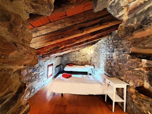 Dormitorio rústico de piedra con camas gemelas en L'Orri Rectoria Nova, Campelles. Vigas vistas y vistas a la montaña.