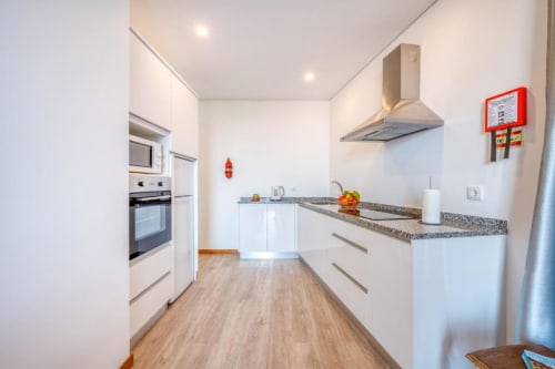 Cozinha moderna branca com bancadas de granito, eletrodomésticos em aço inoxidável e piso de madeira na Villa Amore Accommodation