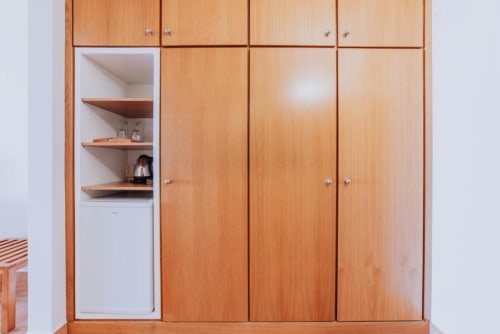Guarda-roupa de madeira com prateleiras abertas exibindo chaleira e artigos de higiene no quarto duplo da Villa Amore